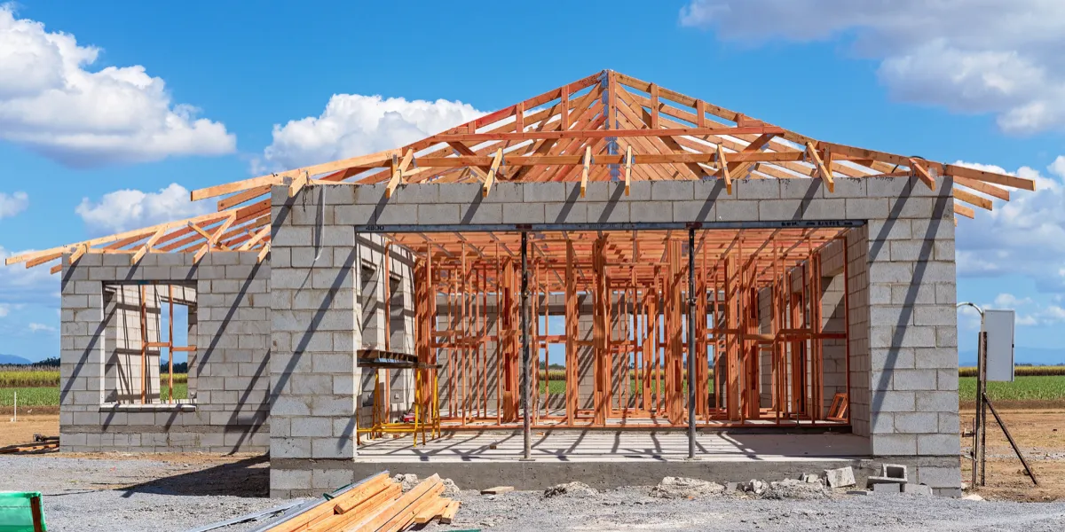 Unfinished house with exposed roof trusses and concrete block walls under a blue sky