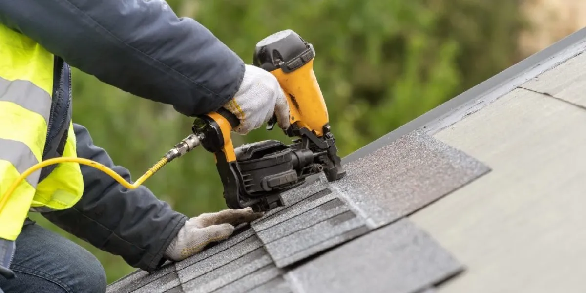 Roofer using a pneumatic nail gun to install asphalt shingles